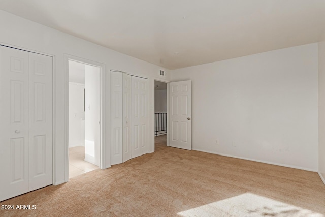 unfurnished bedroom with light colored carpet and two closets