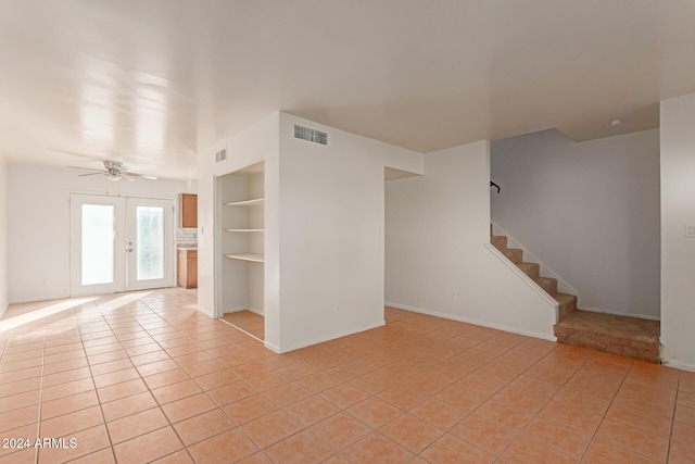 tiled empty room with ceiling fan, built in features, and french doors