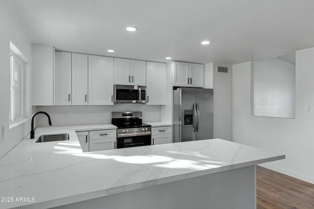 kitchen featuring appliances with stainless steel finishes, white cabinetry, sink, light stone countertops, and light wood-type flooring