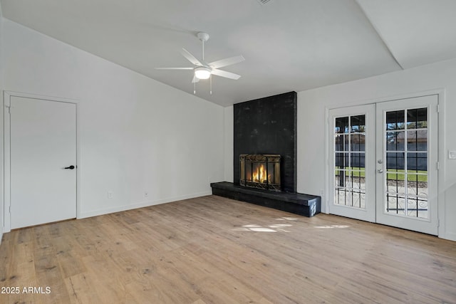 unfurnished living room featuring a large fireplace, light hardwood / wood-style floors, french doors, and ceiling fan