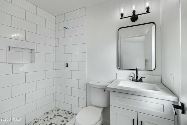 bathroom with tiled shower, vanity, and toilet