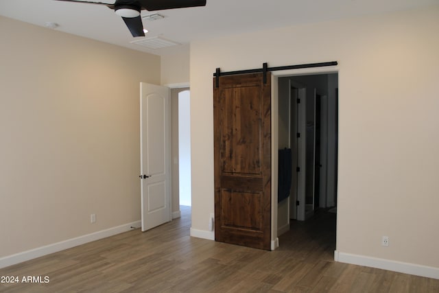 empty room with ceiling fan, hardwood / wood-style floors, and a barn door