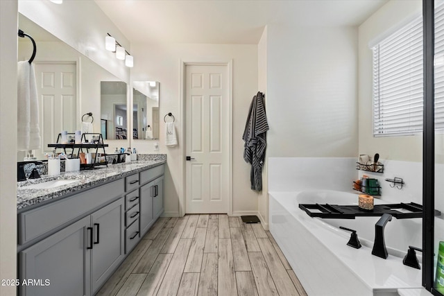 bathroom with double vanity, a sink, a bath, and wood finished floors