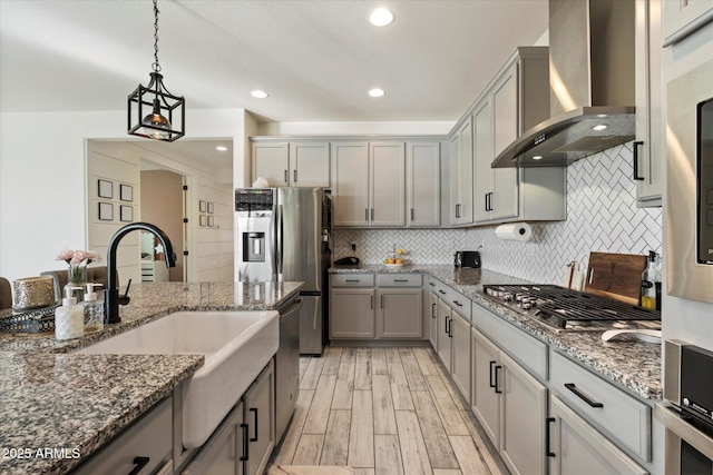 kitchen with gray cabinetry, decorative backsplash, a sink, and wall chimney exhaust hood