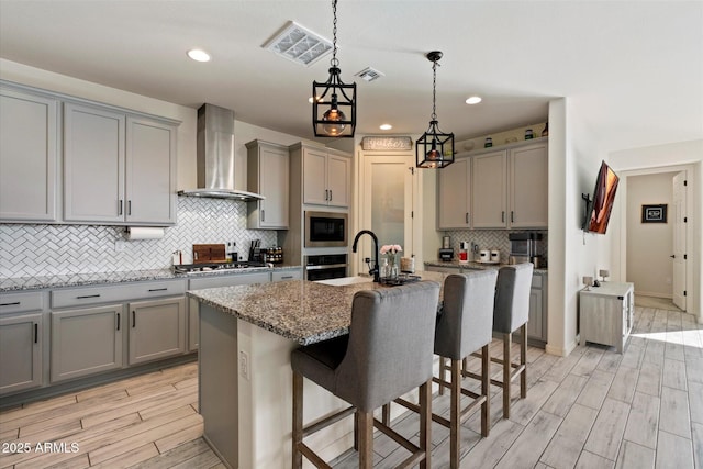 kitchen featuring wall chimney range hood, appliances with stainless steel finishes, light wood-style floors, gray cabinets, and visible vents