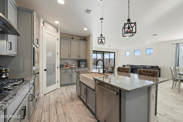 kitchen with a sink, gray cabinets, light wood-style flooring, stainless steel appliances, and visible vents