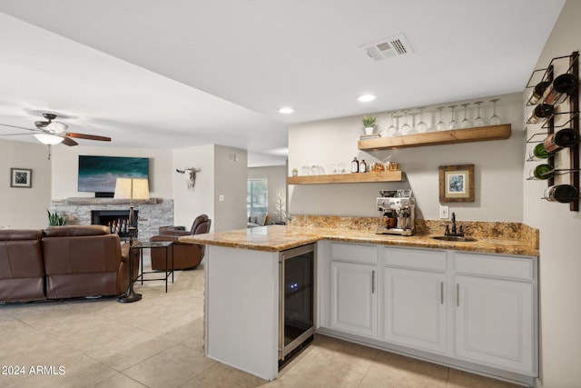 kitchen featuring a stone fireplace, white cabinetry, sink, wine cooler, and kitchen peninsula