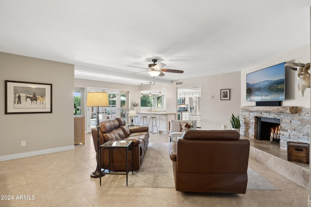 tiled living room featuring a stone fireplace and ceiling fan