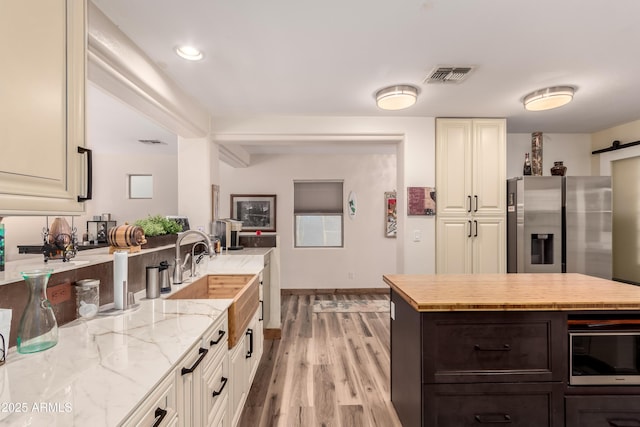 kitchen with sink, light hardwood / wood-style flooring, appliances with stainless steel finishes, a barn door, and light stone countertops