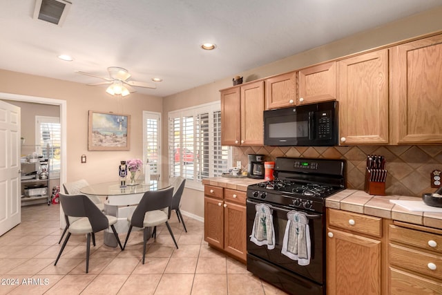 kitchen with black appliances, tile counters, light tile patterned flooring, and tasteful backsplash