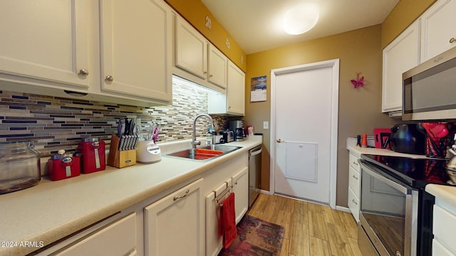 kitchen with light hardwood / wood-style floors, white cabinets, sink, backsplash, and appliances with stainless steel finishes