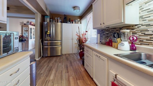 kitchen featuring stainless steel appliances, light hardwood / wood-style floors, white cabinets, and decorative backsplash