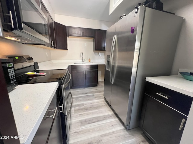 kitchen with dark brown cabinetry, stainless steel appliances, light wood-type flooring, and sink