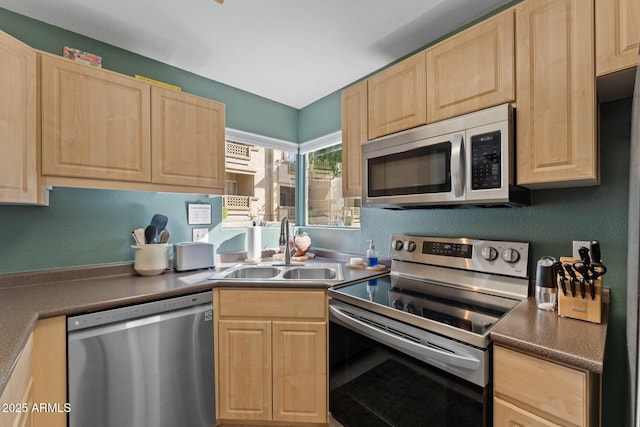 kitchen featuring stainless steel appliances, dark countertops, a sink, and light brown cabinetry