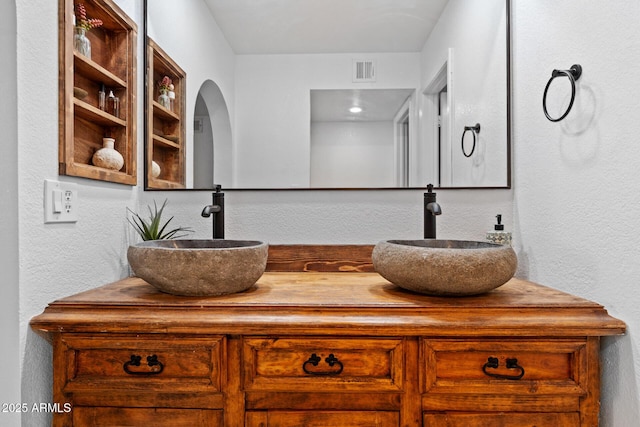 full bath with a textured wall, double vanity, a sink, and visible vents