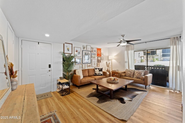 living area featuring light wood-style floors, ceiling fan, and a textured ceiling