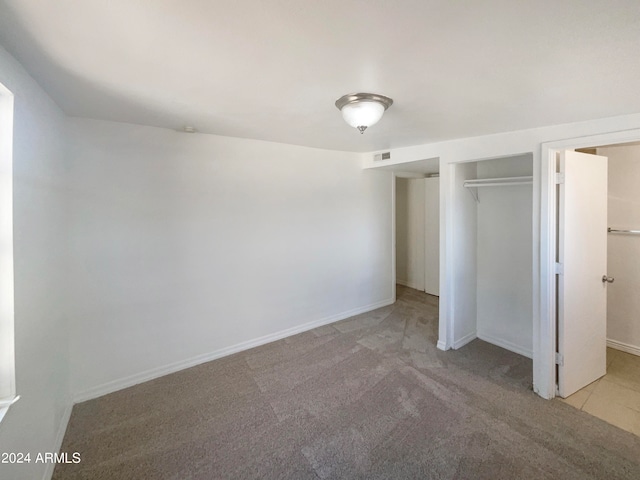 unfurnished bedroom with light colored carpet and a closet