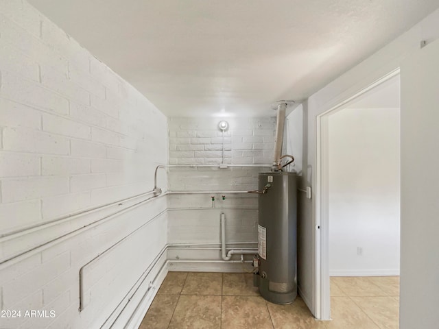 basement featuring water heater, light tile patterned floors, and brick wall