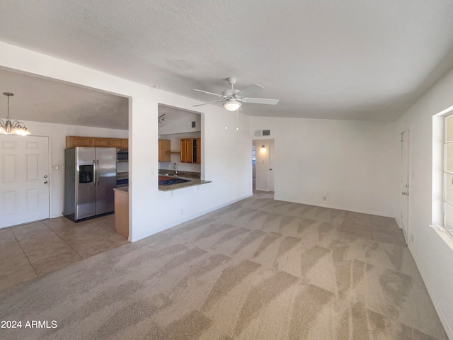 unfurnished living room featuring lofted ceiling, ceiling fan with notable chandelier, sink, a textured ceiling, and light colored carpet