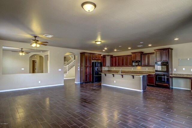 kitchen featuring an island with sink, ceiling fan, a breakfast bar area, and black appliances