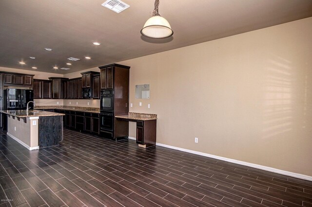 kitchen with black fridge, dark brown cabinetry, a kitchen island with sink, sink, and hanging light fixtures