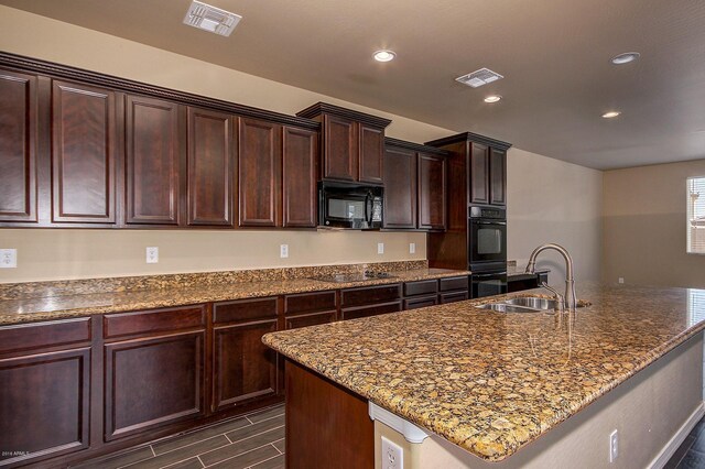 kitchen with black appliances, sink, an island with sink, dark brown cabinets, and light stone counters