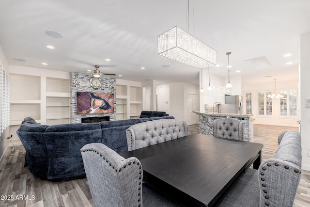 15583 W Big Sky Dr, Surprise, AZ 85374 - dining room featuring built in shelves, a stone fireplace, sink, hardwood / wood-style floors, and ceiling fan with notable chandelier