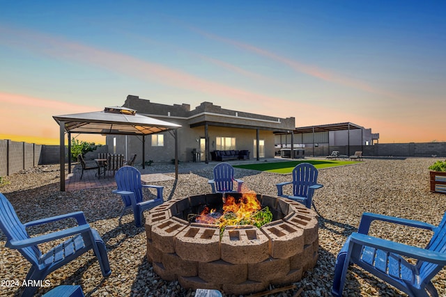 back house at dusk with an outdoor fire pit, a gazebo, and a patio area