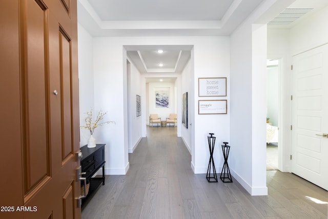 hall with a raised ceiling, baseboards, wood-type flooring, and visible vents