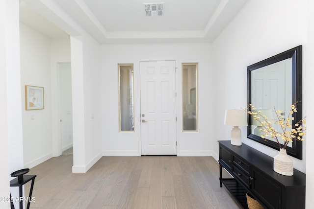 entryway with a raised ceiling, light wood-style floors, baseboards, and visible vents