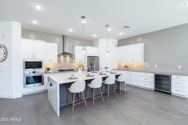 kitchen featuring visible vents, wall chimney exhaust hood, appliances with stainless steel finishes, a kitchen breakfast bar, and wine cooler