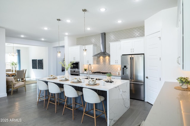 kitchen with wall chimney exhaust hood, a breakfast bar, stainless steel appliances, decorative backsplash, and dark wood-style floors