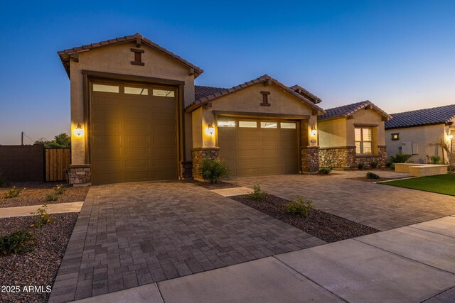 view of front of home with a tile roof, stone siding, a garage, and stucco siding