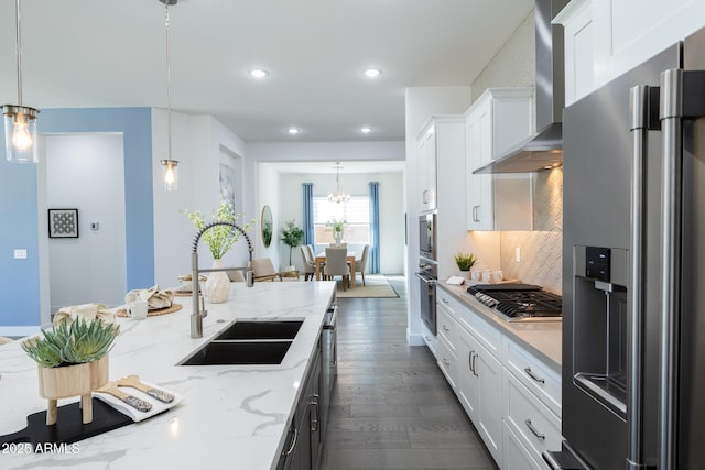 kitchen featuring tasteful backsplash, wall chimney range hood, white cabinetry, appliances with stainless steel finishes, and a sink