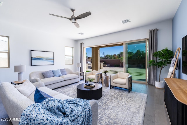 living area featuring visible vents, dark wood-style flooring, a ceiling fan, and a healthy amount of sunlight