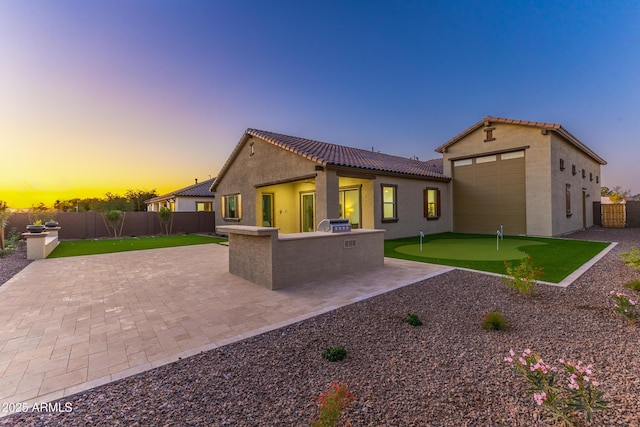 back of property at dusk with a garage, a fenced backyard, a tile roof, a patio, and stucco siding