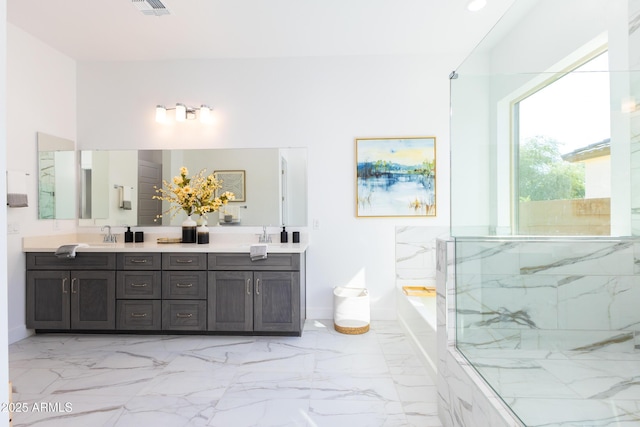 full bath with a sink, double vanity, marble finish floor, and a garden tub