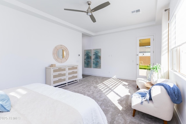 carpeted bedroom featuring baseboards, visible vents, a tray ceiling, and a ceiling fan