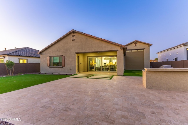 back of house at dusk with a patio, stucco siding, an outdoor structure, and fence private yard