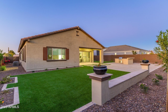 back of house at dusk featuring a yard, a fenced backyard, a patio area, and central air condition unit