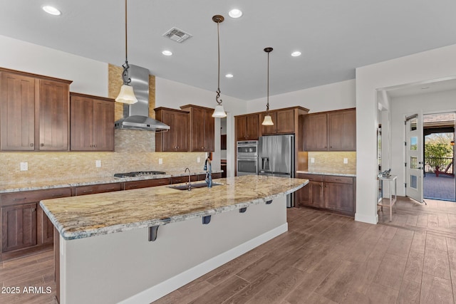 kitchen featuring visible vents, a sink, dark wood-style floors, stainless steel appliances, and wall chimney range hood