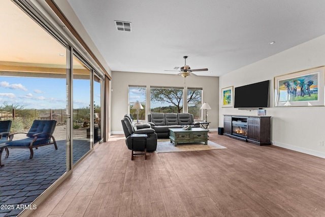 living room featuring a ceiling fan, wood finished floors, visible vents, and baseboards