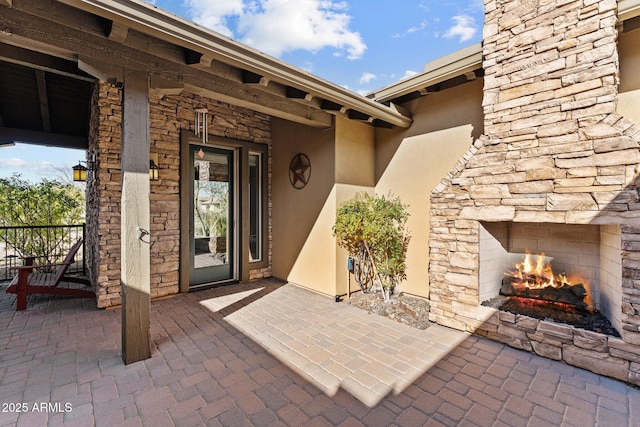 view of exterior entry with a patio area, stone siding, stucco siding, and an outdoor stone fireplace