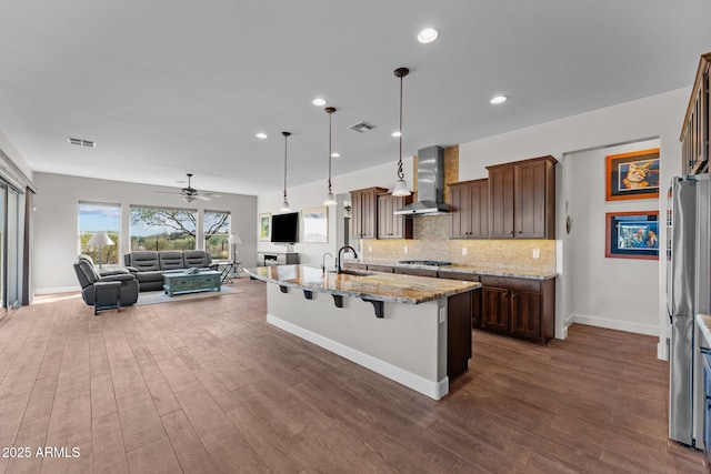 kitchen with visible vents, stainless steel appliances, wall chimney exhaust hood, open floor plan, and backsplash