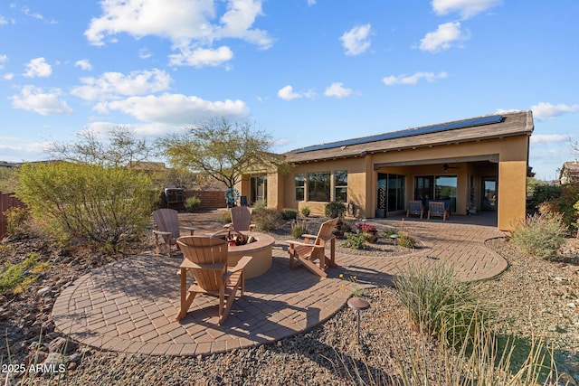 rear view of house featuring stucco siding, a patio, fence, a fire pit, and solar panels