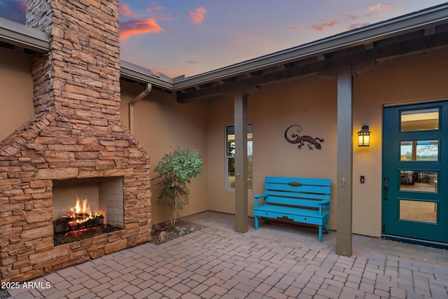 view of exterior entry featuring stucco siding, stone siding, an outdoor stone fireplace, and a patio area