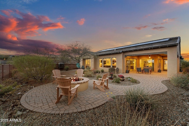 back of property at dusk featuring stucco siding, a patio area, solar panels, and an outdoor fire pit