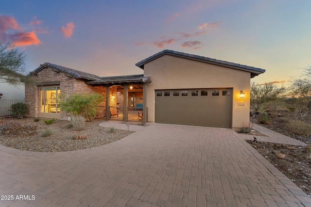 view of front of home featuring fence, an attached garage, stucco siding, stone siding, and decorative driveway