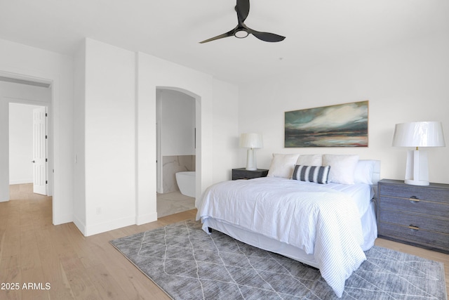 bedroom featuring baseboards, ceiling fan, connected bathroom, wood finished floors, and arched walkways