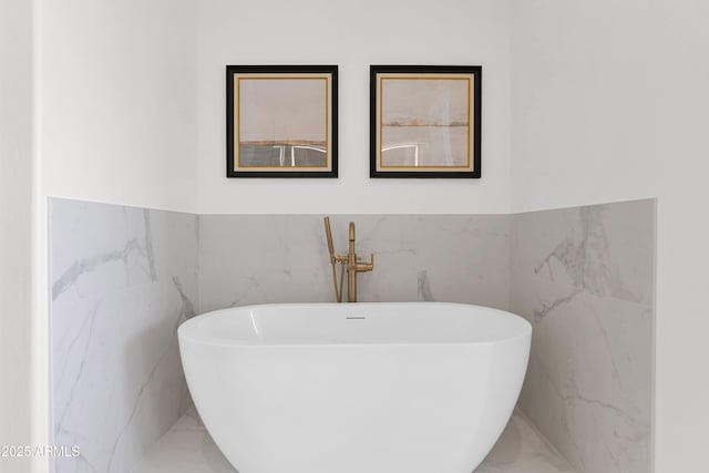 full bath with wainscoting, a freestanding bath, tile walls, and marble finish floor